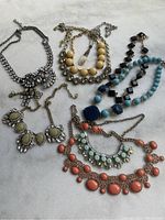 Seven assorted costume jewelry necklaces arranged on a white surface showing various colors and styles.