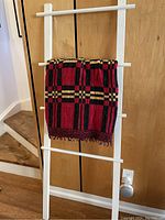 Heavy cotton blanket draped over the third rung of the white wooden ladder, showing the fabric pattern and colors