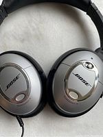 Close-up of Bose QuietComfort 15 headphones showing silver ear cups with Bose logo and model name.