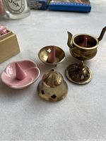 Photo of three brass incense holders, two incense cones placed inside two holders, and a pink ceramic dish holding an incense cone
