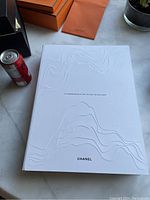White hardcover Chanel coffee table book titled 'Le Laboratoire A Ciel Ouvert De Baljac' on a marble surface.