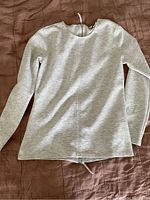 Front view of the light gray long sleeve top laid flat against brown background showing round neck and overall fit.
