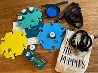 Overview photo showing the FluentPet puzzle piece boards in yellow, teal, and blue, several talking button units on top, two black leashes, blue collapsible bowl, and canvas tote bag.