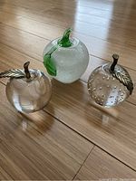 Three decorative glass apples including one with green leaf, one with metallic leaf and air bubbles, and one clear with metallic leaf.