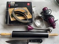 Overview photo of the lot including Zwilling J.A. Henckels meat cutter in box, rolling pin, chef's knife, and immersion blender parts