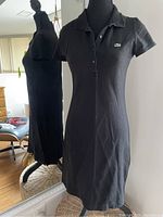 Front and side view of black Lacoste polo dress on mannequin, showing collar, buttons and logo.
