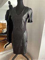 Front view of the black lambskin leather dress on mannequin, showing V-neck and short puff sleeves.