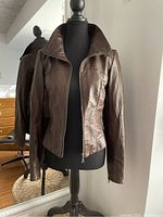 Front view of butter soft dark brown leather jacket on mannequin, slightly fitted, with zipper front and stand-up collar.