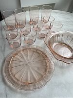 Pink glass bowl, cake stand, 4 tall glasses, 6 smaller cups on white surface