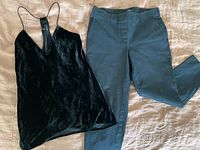 Black velvet tank top laid flat next to black pants on a bed, showing full front view of both items.