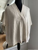 Front view of a beige cashmere sweater displayed on a mannequin showing V-neck and loose sleeves
