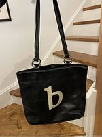 Full view of black leather purse with shoulder straps and white 'b' stitched on front.
