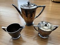 Photo showing three pieces of vintage tea set: teapot, creamer, and sugar bowl arranged on wood floor.