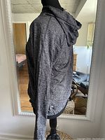 Side view of a dark heathered gray Lululemon women's jacket with hood on a mannequin in a room with mirror.