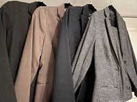 Five women's suit jackets in varying neutral shades hanging on hangers, showcasing the range of styles and colors.
