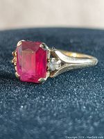 Close-up image of the red garnet stone set in a gold ring with one small side stone missing.