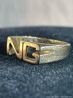 Front angled view of ring showing raised NG letters and textured band