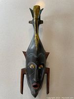 Full front view of carved wooden Kpelie mask showing elongated form, perching bird, cheek projections