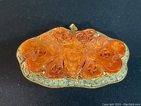 Full view of vintage butterfly pendant showing carved orange stone and brass inlay border on black background.