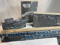 Four assorted vintage wood and lead printers blocks shown together on a neutral background, displaying reversed embossed text and detailed architectural illustrations.