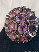 Front view of the vintage purple glass brooch showing faceted stones in ornate brass-tone metal setting.