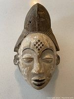 Front view showing carved facial features, painted worn surface, and tall headpiece with linear textures and cross marks.