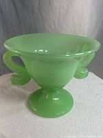 Full front view of the green jadeite Fenton candy bowl featuring flared rim and dolphin handles.