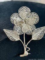 Front view of vintage filigree silver flower brooch on black background.