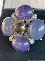 Close-up front view showing four large oval stones in purple and blue shades with a faceted brown center stone and smaller light blue rhinestone accents.