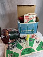 Full lot including the fishing reel with line, the original box, instruction manual, and parts list spread out in front of the box.