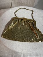 Gold tone mesh evening purse with chain handle displayed on white fabric background.
