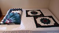 Photo of the bedding set including 2 folded floral patchwork duvets and 2 pillowcases placed on a bed with white sheet.