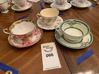 Photo showing three tea cups and saucers with different floral designs and gold accents on a wooden table.