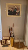 Overall view of umbrella stand with umbrellas and canes, framed botanical prints, glass top side table and floral artwork above.
