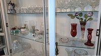 Display cabinet with multiple glass, ceramic, and crystal decorative items including bowls, vases, and figurines.