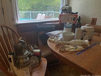 Wide view of the kitchen appliances lot on dining room table and chair including food processor, blender, mixer, soda syphon, fry pan, induction cooktop, and carver.