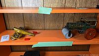 Two pressed tin toys on orange shelf, yellow and blue U.S. Army plane, black and green tractor roller with red wheels