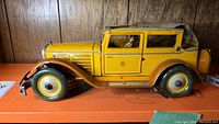 Full side view of the yellow pressed tin toy car showing body shape, wheels, and windshield.