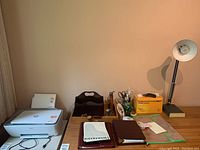 Overview of printer, paper, letter sorter, office supplies, notebooks, and desk lamp on wooden desk.