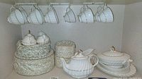 Overall view of hanging teacups, storage tins and tea service pieces on shelf