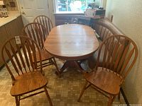 Wooden oval dining table with four matching chairs in a kitchen nook setting, showing natural wood grain and style.