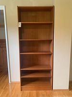 Front view of the tall teak bookshelf showing all six shelves and some visible surface marks.