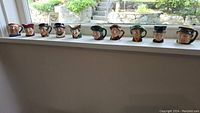 Photo of 10 miniature Toby mugs displayed on a window sill, showing varied character faces with different hats and expressions
