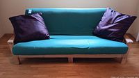 Full front view of wood frame futon couch showing green cushion and two purple pillows.