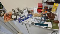 Photo showing assortment of vintage advertising items, new candle, ceramic baseball glove, and various stationery items on a countertop