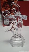 Crystal dancer figurine of dancing couple with one arm raised, standing on a stepped rectangular base, with red box in background.