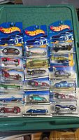 Photo showing 17 Hot Wheels cars in unopened packaging arranged in rows on a green surface.