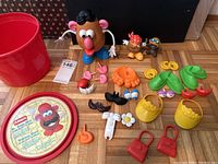 Full lot overview showing Mr. Potato Head figure, various accessories including facial features and clothing pieces, two small character toys, red storage bucket, and red storage lid.