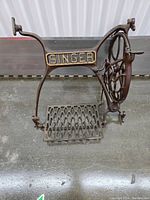 Side view of the Singer sewing machine treadle base showing the foot pedal and flywheel mechanism.