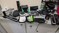 Image of assorted electronics and accessories including Amazon Echo Dot, desk vacuum, power banks, sleep machine, cables, and other small devices arranged on a countertop.